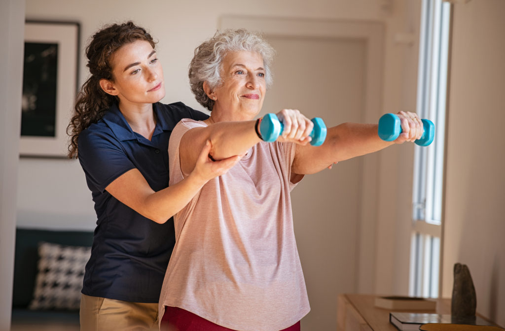Senior women using dumbbells to perform physical therapy exercises with trainer