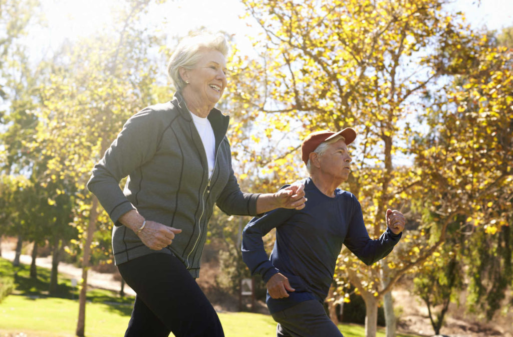 A senior man and woman jogging in the park to keep themselves physically active and healthy.
