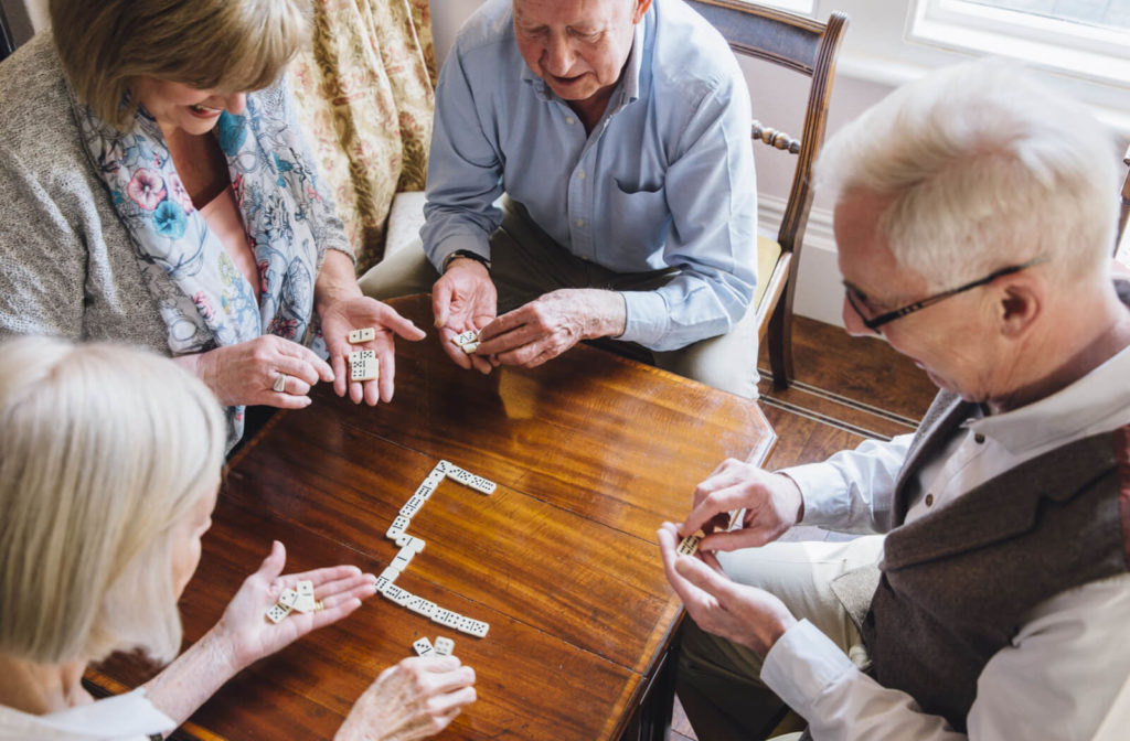A group of elderly people in a retirement home are sitting around the table playing Domino.