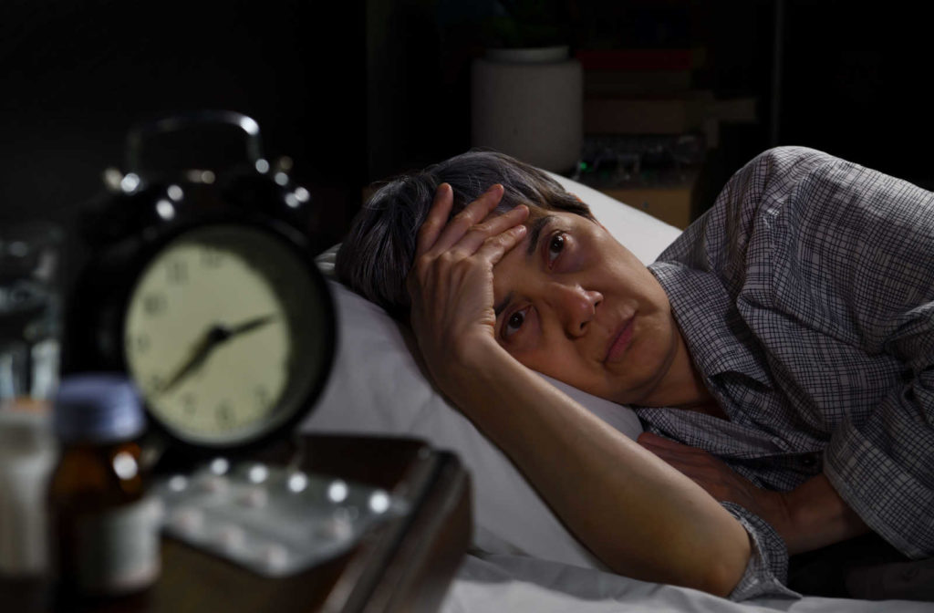 A senior woman lying in bed holding her head as she finds it difficult to fall asleep at night. Seniors face insomnia and may need help to fall asleep.